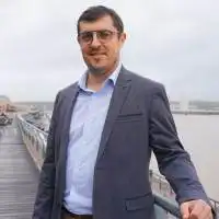 Homme en costume sur un pont par temps gris.