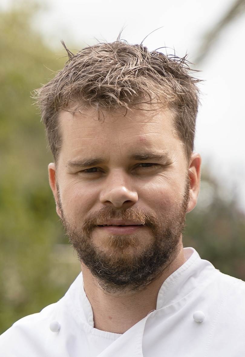 Chef souriant en veste blanche, extérieur flou.