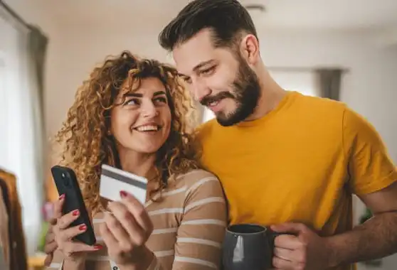 Couple souriant avec carte de crédit et téléphone.