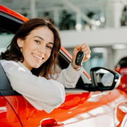 Femme souriante tenant clé dans voiture rouge.